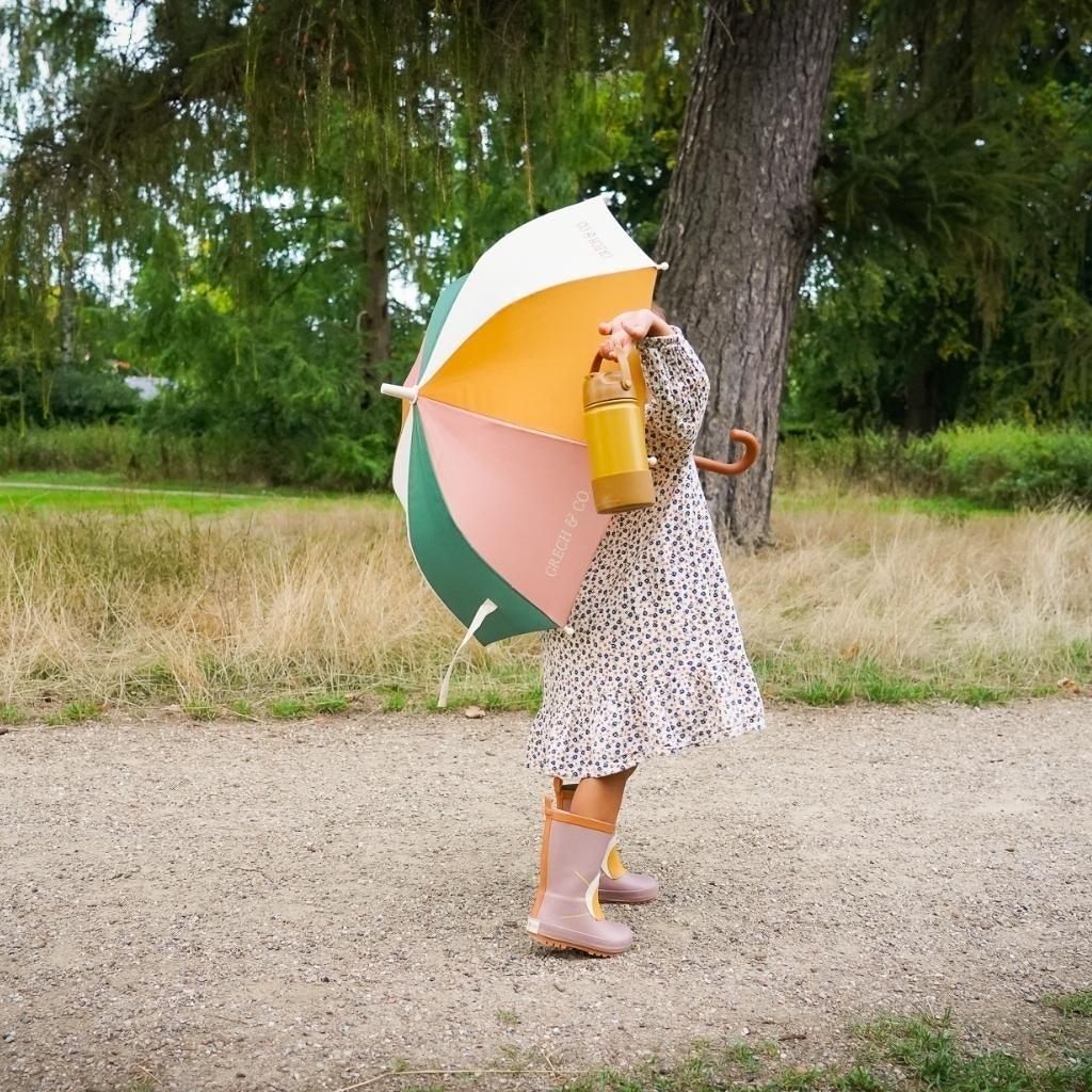 The umbrella held by a little girl fully opened. She is standing on. footpath with grassland and trees in the background.
