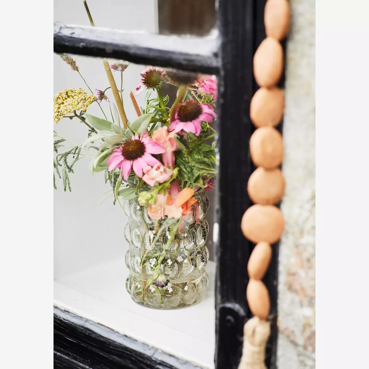 Glass vase filled with flowers from the garden placed on a windowsill.